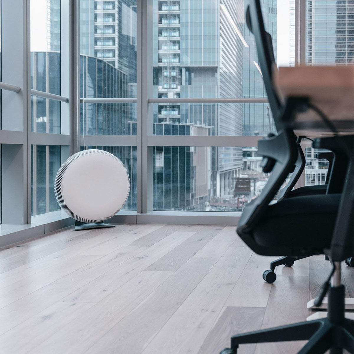 IQAir Atem X Luftreiniger, weiß, rund, in einem Büro vor Fensterfront mit Blick auf Hochhäuser