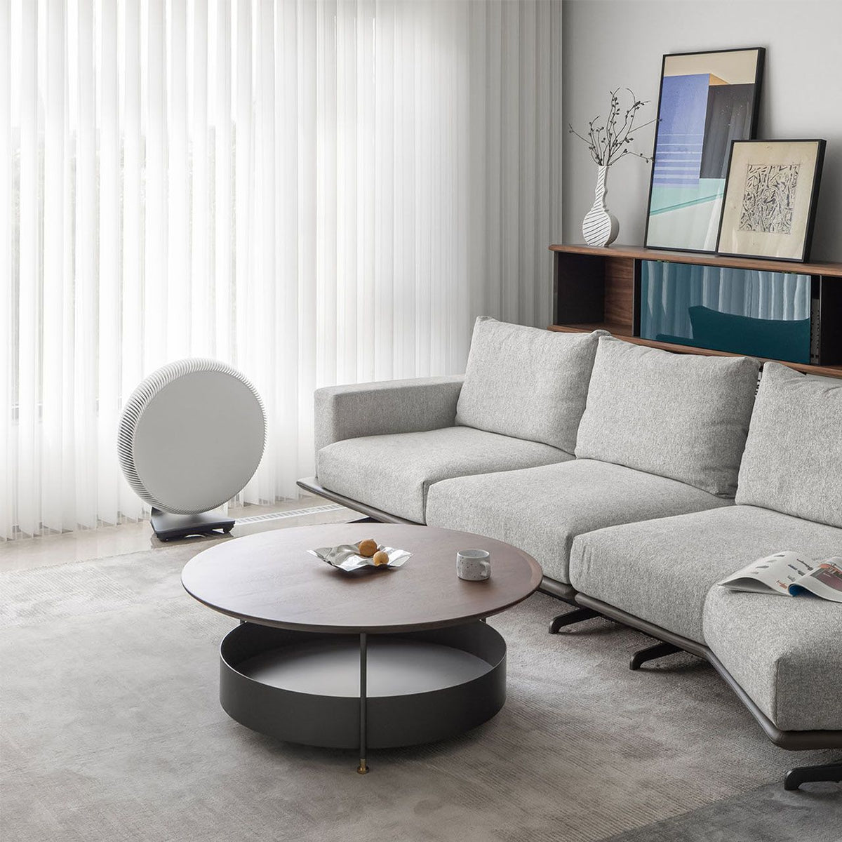 IQAir Atem X Luftreiniger, rundes weißes Gerät neben Sofa im Wohnzimmer vor Vorhang