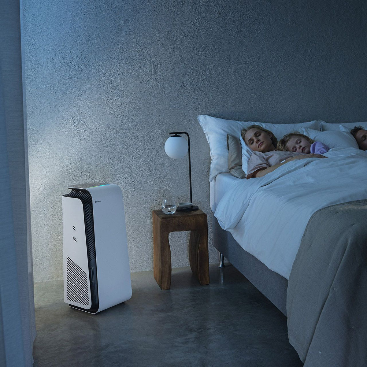 Blueair HealthProtect 7740i Luftreiniger neben Bett mit schlafender Familie im abgedunkelten Schlafzimmer